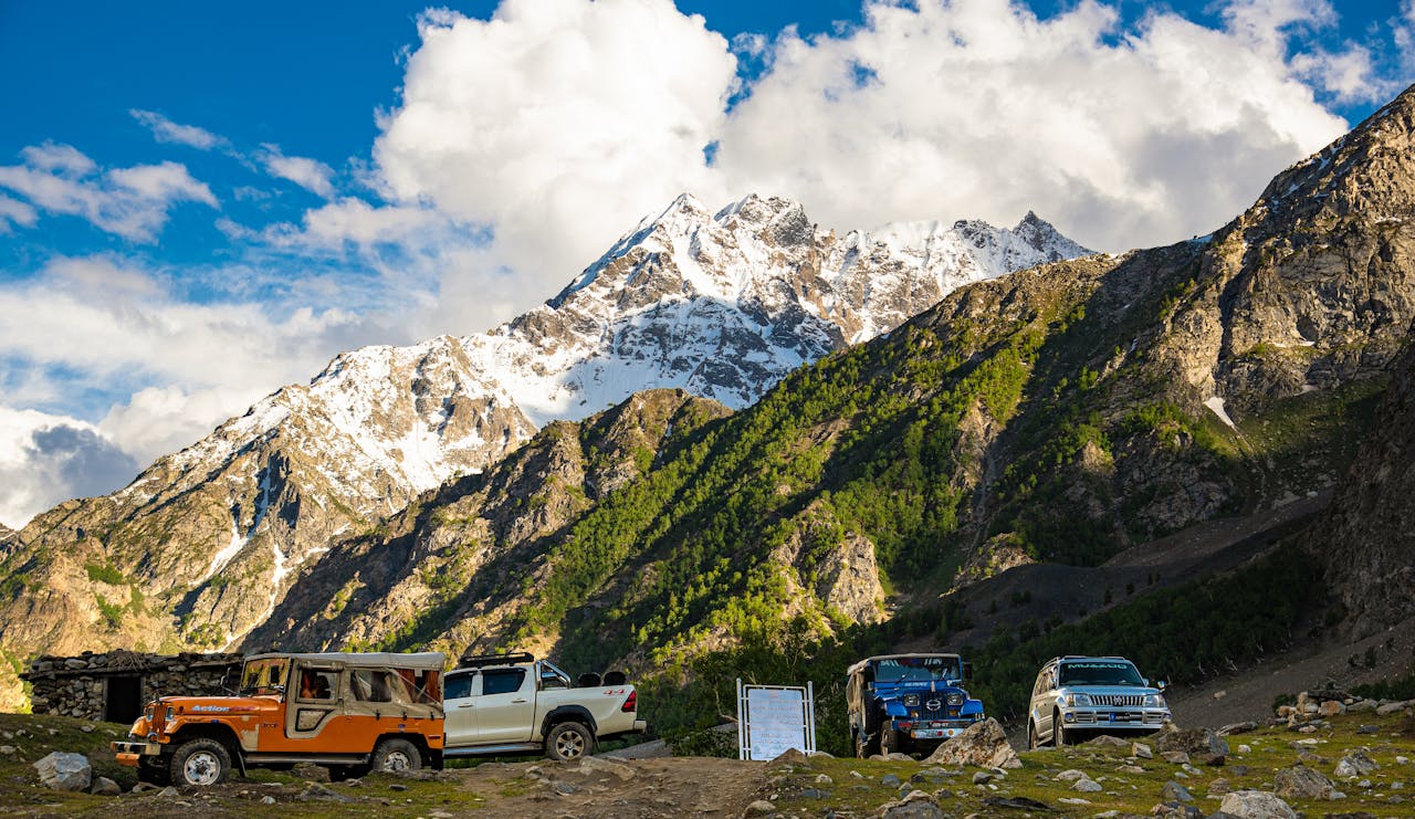 Stunning snow-capped mountains and vehicles in Naltar Valley, a perfect adventure landscape.